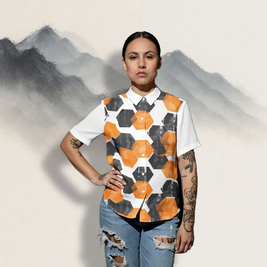 A woman wearing the HexaFlux Geometric Button-Up Shirt, standing confidently in front of a soft sumi-e mountain background, showing the bold orange and black hexagon pattern.