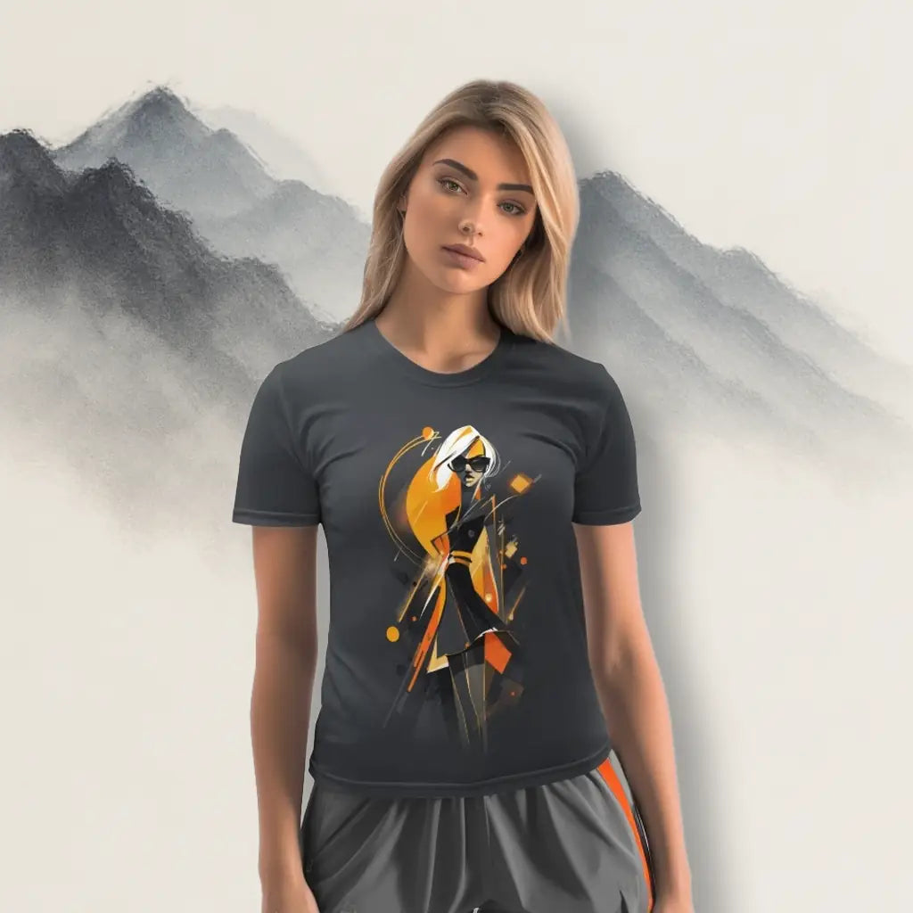 Female model wearing a dark grey t-shirt with a stylized figure and abstract print in orange, black, and white, standing against an artistic mountain backdrop. Shows the t-shirt's fit and lifestyle context as wearable art.
