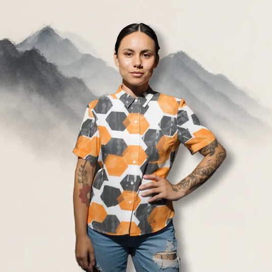 A woman wearing the HexaFlux Geometric Button-Up Shirt, standing confidently in front of a soft sumi-e mountain background, showing the bold orange and black hexagon pattern.
