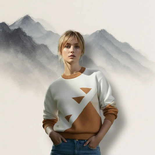 Studio shot of the Desert Geometry jacquard sweater by Haven of Dreams, modeled against a minimalist mountain backdrop. Features terracotta triangle motif on cream cotton blend.
