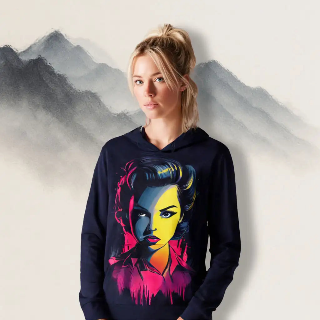 A woman wearing the Neon Femme Portrait Hoodie in front of misty watercolor mountains, highlighting the vibrant pop-art face design.