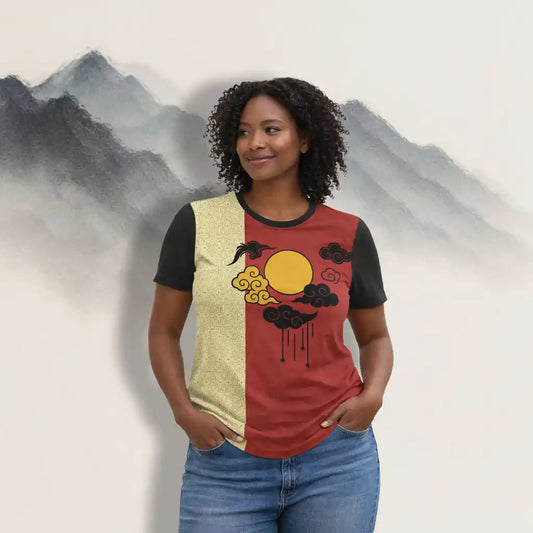 Woman wearing a red and black graphic t-shirt with a yellow sun and cloud illustration, styled with blue jeans, on a misty mountain backdrop.