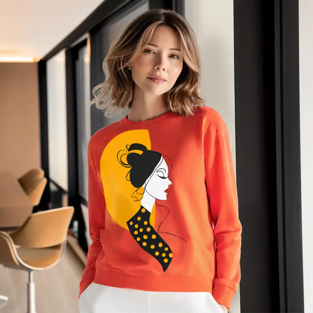 Lifestyle photo of a woman in a bright, modern interior wearing the orange 'Sunset Muse' graphic sweatshirt, showing how the art print adds a pop of color and sophistication.